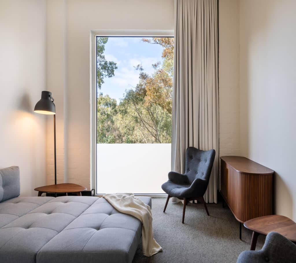 A room with tall ceiling, floor-to-ceiling windows with full drapes, and a fold-out bed.