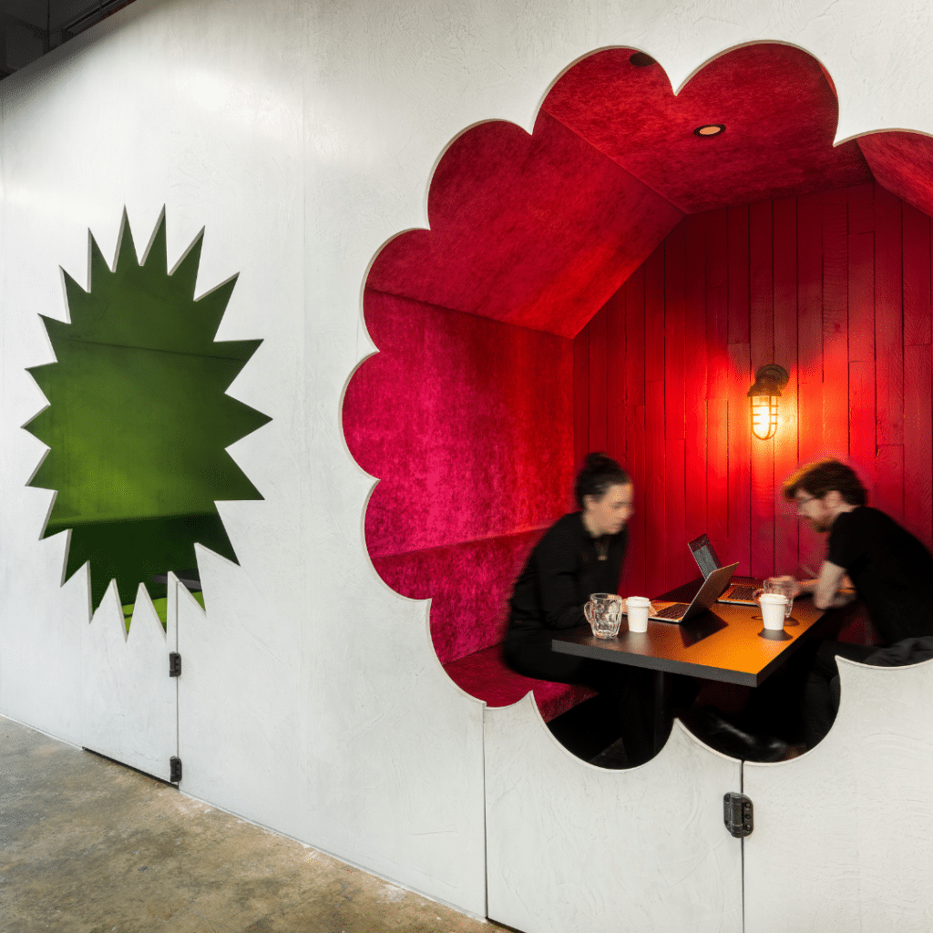 Two coworkers in a pink velvet lined collaboration booth.