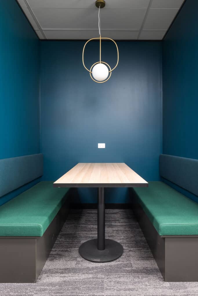 Navy blue walls surround a booth of emerald green, with a timber table and pendant light.